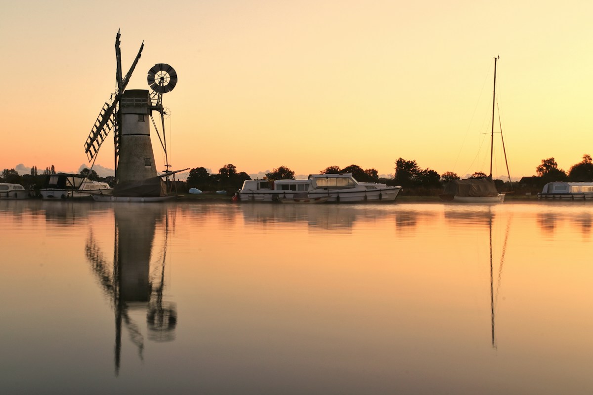 A traditional drainage windmill on the Norfolk Broads at sunset, with moored boats
